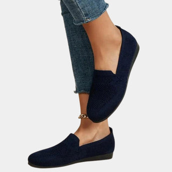 Women's dark blue denim flats with a chain ankle bracelet detail, worn by a model showcasing the casual footwear style.