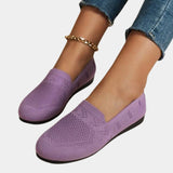 A pair of women's purple denim flats featuring a chain ankle bracelet, shown on a person wearing blue denim pants.