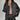 Women's designer leather jacket in black, featuring a bow motif and metallic stripes. The jacket includes a collar, long sleeves, and fits at the waist, showcasing a fashionable and stylish outerwear piece.