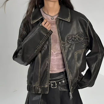 Women's designer leather jacket in black, featuring a bow motif and metallic stripes. The jacket includes a collar, long sleeves, and fits at the waist, showcasing a fashionable and stylish outerwear piece.