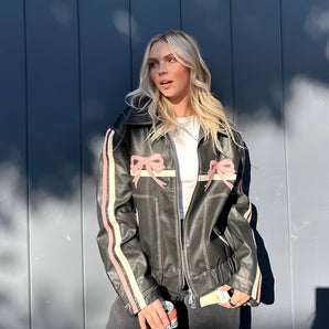 Women's designer leather jacket featuring a bow motif and metallic stripes, with a focus on the sleeve, waist, thigh, and collar areas, styled in a fashion-forward manner.
