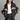 Black women's designer leather jacket featuring a pink bow motif and metallic stripes. The jacket has a stylish collar and shoulder design, with long sleeves. Fashionable and cool, it is paired with black hair, highlighting its chic appearance.