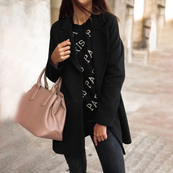 A woman wearing a chic black double-breasted long winter coat, featuring a tailored fit with prominent shoulders, a stylish collar, and full-length sleeves. The coat is complemented by casual accessories and is marked as a 5XL size, showcasing an urban fashion style.