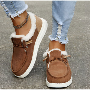 Brown corduroy winter loafers with faux fur lining are shown being worn by a person. The loafers are paired with jeans, highlighting their casual and warm design, suitable for cold weather.