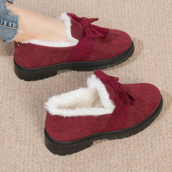 Women's red faux fur-lined suede loafers with bow tie detailing on top, shown with a human leg for scale.