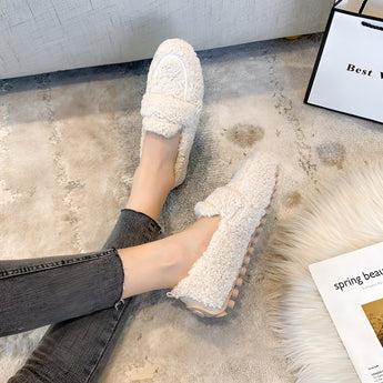 Beige women's fluffy slippers with a plush, non-slip sole on a wooden floor, designed for warmth and comfort during winter.
