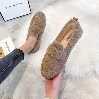 
A pair of women's fluffy slippers in a warm cachi color, designed for non-slip comfort in winter, displayed on a wooden surface.