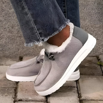 Women's gray fleece-lined winter loafers on feet, shown outdoors on grass, showcasing their stylish slip-on design and warm lining, ideal for cold weather.