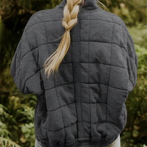 Women's gray lightweight quilted jacket with long sleeves and waist-length design, displayed outdoors in a natural setting with grass in the background.