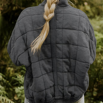 Women's gray lightweight quilted jacket with long sleeves and waist-length design, displayed outdoors in a natural setting with grass in the background.