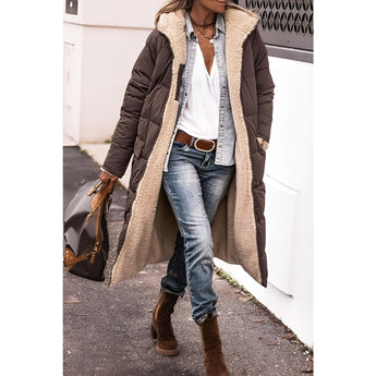 
A woman wearing a gray sherpa-lined insulated parka styled for urban winter use. The coat features a warm lining and a fashionable design, paired with jeans and a hat for a complete winter outfit.