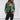 
A fashionable woman wearing a green suede moto jacket in a trendy spring style, featuring a structured collar and long sleeves, paired with casual attire. The model is posing confidently, highlighting the jacket's design and fit, suitable for plus-size fashion, specifically size 5XL.