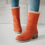 Women's green suede shearling block heel ankle boots with a hint of orange on the trim, displayed on a model's foot. The boots feature a stylish and warm design suitable for colder weather.