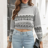 Women's grey cropped turtleneck Aztec sweater, featuring a modern knitwear design. The model is wearing sunglasses and poses with a stylish hairstyle, showcasing the sweater's outerwear appeal.
