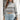 Women's grey cropped turtleneck Aztec sweater, featuring a modern knitwear design. The model is wearing sunglasses and poses with a stylish hairstyle, showcasing the sweater's outerwear appeal.