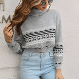 
A woman wearing a grey cropped turtleneck sweater with an Aztec pattern, styled with jeans, and accessorized with glasses.