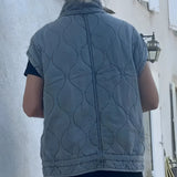 Women's grey sleeveless quilted puffer vest, lightweight and perfect for winter layering, shown on a model wearing a blue T-shirt and denim jeans.