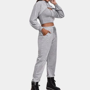 
A woman wearing a grey tracksuit set consisting of a cropped hoodie and joggers, styled for urban athleisure.