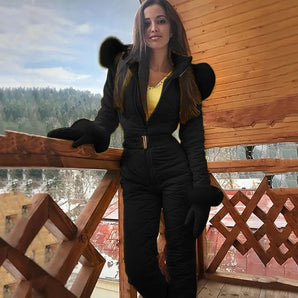 Women's insulated black hooded winter jumpsuit, featuring a stylish design suitable for ski fashion, with focus on sleeve and waist detailing, photographed against a cloudy sky.