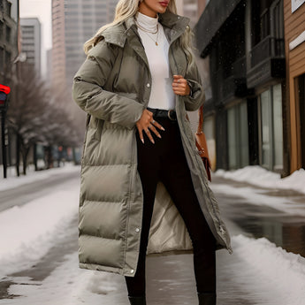 Olive green women's insulated puffer coat in 3XL size, featuring a long design with a hood, suitable for winter. The coat has a stylish overcoat look with a waist belt and fur-lined hood, set in a snowy outdoor scene.
