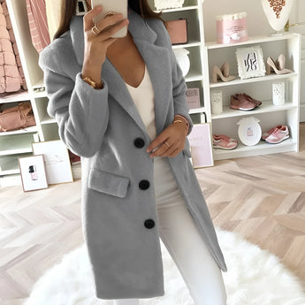 
A woman modeling a long black double-breasted blazer, tailored for an office chic look. The blazer features a structured collar, long sleeves, and is shown in a gray color, size 4XL. The model's hand is placed on her waist, highlighting the fashion-forward design and fit of the blazer.