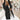 
Image of a woman wearing a long black oversized blazer in a tailored chic fashion style. The blazer features long sleeves and a structured collar, paired with a dress shirt. The woman is gesturing with her hand near the waist and is wearing eyewear. The blazer is in a 5XL size, providing a stylish and comfortable fit.