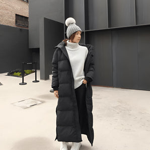 Women's long black puffer coat with a hood, designed for urban winter wear, featuring a stylish waist-cinched silhouette and knee-length coverage.