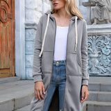 Women's long blue oversized zip-up hoodie modeled in an urban streetwear style. The image features the hoodie with long sleeves, a high neck, and a relaxed fit, worn by a woman standing confidently. She is accessorized with sunglasses, emphasizing a trendy and fashionable look. The overall color palette includes hints of black and white elements.