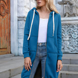 Women's long oversized zip-up hoodie in a vibrant blue color, styled as urban streetwear. The hoodie is worn by a model standing confidently, with the garment featuring a hood, long sleeves, and a relaxed fit.