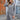 
A woman wearing a long blue oversized zip-up hoodie, styled in an urban streetwear fashion, standing outdoors. The hoodie features long sleeves and a high collar. She is accessorized with sunglasses, complementing the casual and trendy look.