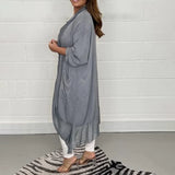 A woman wearing a long, flowy grey kimono cardigan, designed as a versatile summer wrap, showcasing its elegant drape over the shoulders and arms with loose sleeves, emphasizing a casual yet stylish look.