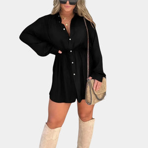 A woman wearing a long-sleeve black shirt dress with a casual and versatile design, featuring a mini dress length. She is accessorized with sunglasses and has her hair styled simply.