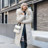 Women's long winter coat with fur hood, shown in white color and 3XL size, featuring quilted insulation, highlighting the overcoat's design elements such as the fur-trimmed collar, full-length sleeves, fitted waist, and overall parka style. The background includes a window, adding natural light to the setting.