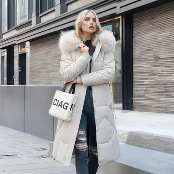 Women's long winter coat with fur hood, shown in white color and 3XL size, featuring quilted insulation, highlighting the overcoat's design elements such as the fur-trimmed collar, full-length sleeves, fitted waist, and overall parka style. The background includes a window, adding natural light to the setting.