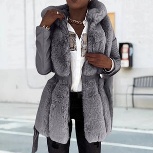 Woman wearing a stylish grey faux fur hooded parka with long sleeves, standing in an upright position. The parka extends to thigh length, featuring a luxurious design ideal for winter wear.
