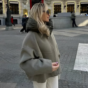 
A woman wearing an oversized green high-collar hoodie, styled for urban fashion, standing on a sidewalk. The hoodie is in a light green color and size large, featuring long sleeves and a relaxed fit, ideal for a casual and stylish outdoor look.