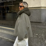 Women's oversized green high-collar hoodie with long sleeves, styled as urban fashion. The model is accessorized with sunglasses, showcasing a modern and trendy look.