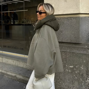 Women's oversized green high-collar hoodie with long sleeves, styled as urban fashion. The model is accessorized with sunglasses, showcasing a modern and trendy look.