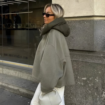 Women's oversized green high-collar hoodie with long sleeves, styled as urban fashion. The model is accessorized with sunglasses, showcasing a modern and trendy look.
