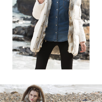 Women's luxury white puffer jacket with a fur hood, showcasing the front view with a high collar and long sleeves, photographed in a fashion setting.