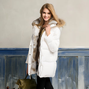 White puffer jacket with fur hood worn by a woman standing and smiling, showcasing the coat's luxurious design and winter style.