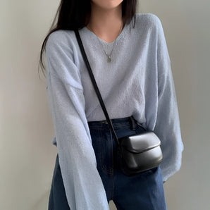 Compact blue leather crossbody bag worn by a person dressed in a grey outfit, showcasing its minimalistic and trendy design.