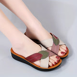 Women's multicolor leather wedge heel sandals with open-toe design, worn on a woman's feet, showcasing stylish and comfortable footwear.