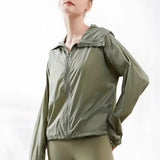 Woman wearing an olive green hooded windbreaker, lightweight and breathable with a zip-up front, in a size large.