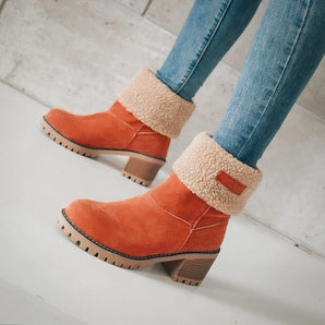 Women's orange suede ankle boots featuring a sherpa lining and chunky heel, shown on a person’s feet.