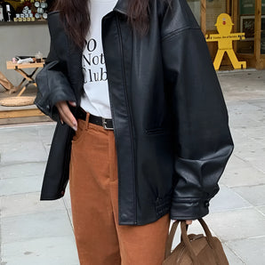 Women's oversized black leather jacket in a casual street style fashion, featuring a structured shoulder and long sleeves, worn by a person standing and showcasing modern outerwear styling.
