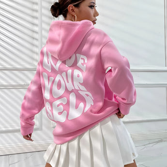 
A woman wearing an oversized pink pullover hoodie. The hoodie is styled as a piece of loungewear, featuring a comfortable and relaxed fit with long sleeves and a roomy neckline.