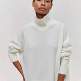 
A woman wearing an oversized black turtleneck sweater with long sleeves, showcasing a casual winter look. The sweater is made from a soft jersey material and fits loosely around the waist and neck, providing a cozy and comfortable style.
