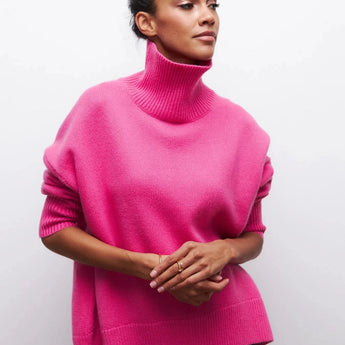 
A woman wearing an oversized black turtleneck sweater, suitable for casual winter wear. Her facial expression is calm, and she is gesturing with her arm. The sweater features long sleeves and is styled comfortably around her neck.