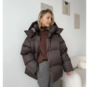 
A stylish women's oversized hooded puffer jacket in brown, showcasing trendy winter fashion with a comfortable fit. The jacket features long sleeves, a waist-length design, and a high collar, providing ample warmth and coverage.
